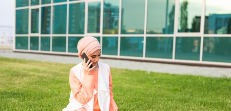 Smiling businessman talking on a cell phone in Dubai. Arab hijab goovrit businessman on cell phone on the street on a background of skyscrapers of Dubai. The woman is dressed in a black abayaの写真素材