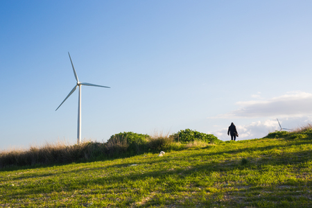 green meadow with Wind turbines generating electricity and man going into the distanceの写真素材