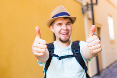 Handsome bearded tourist with backpack is making travel across city. Man standing and giving thumb up.の写真素材