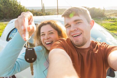 Auto business, car sale, deal and people concept - Happy funny beautiful couple shows key with new car on backgroundの写真素材