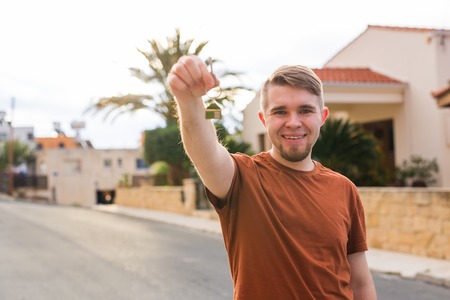 New home, apartment, owner and people concept - Close up of keys that showing young happy man with new home on backgroundの写真素材