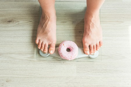 Diet Concept. Close-up of Womans feet On Weighing Scale With Donut. Concept of Sweets, Unhealthy...