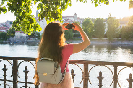Woman taking pictures with smartphone. Stylish summer traveler woman in hat with camera outdoors in european city, Czech Republic, Europeの写真素材