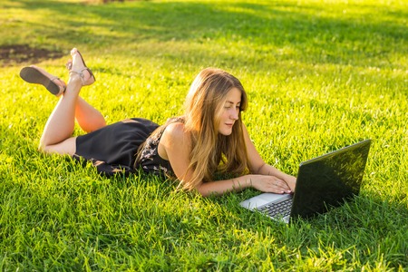 Young woman using laptop in the park lying on the green grass. Leisure time activity conceptの写真素材