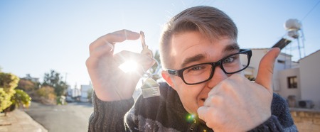 Portrait of a young funny man holding new house key and gesturing thumbs up - new home or apartment conceptの写真素材