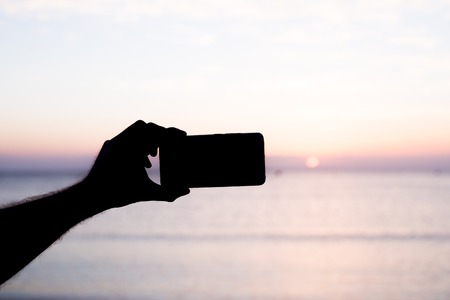 silhouette hand holding smartphone take photo at sunsetの写真素材