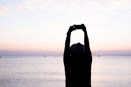 man taking photos of sunset with mobile phoneの写真素材