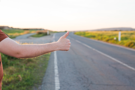 road trip, travel, gesture and people concept - man hitchhiking and stopping car with thumbs up gesture at countrysideの写真素材