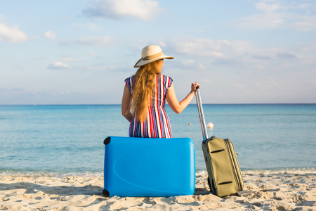 Beach, Holiday, Vacation and Happiness Concept - young woman near the sea with her luggage, rear viewの写真素材
