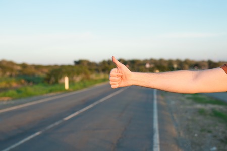 road trip, travel, gesture and people concept - man hitchhiking and stopping car with thumbs up gesture at countryside.の写真素材