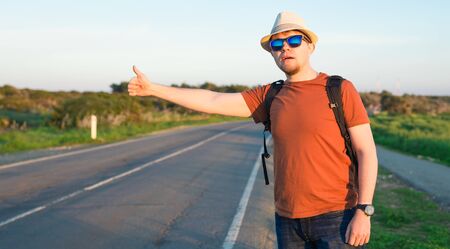 Hitchhiking traveler try to stop car on the mountain road.の写真素材