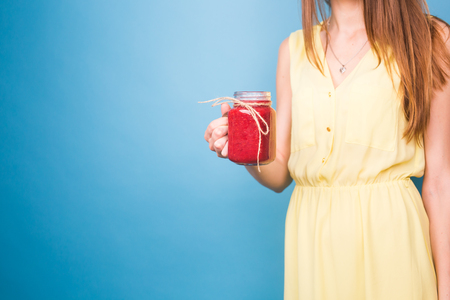 Beautiful young woman holding strawberry smoothie on blue background. Healthy organic drinks...