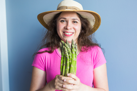 Close-up portrait of funny surprised woman is holding asparagus in front of her face.の写真素材