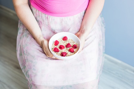 Woman's hands hold healthy and natural breakfast, oatmeal and raspberries in a bowl.の写真素材