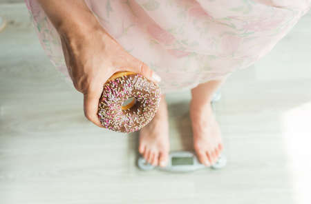 Diet Concept. Close-up of Womans feet On Weighing Scale With Donut. Concept of Sweets, Unhealthy Junk Food and obesity.の写真素材