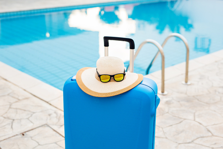 Travel, vacation and holiday concept - Blue suitcase, hat and sunglasses near swimming poolの写真素材