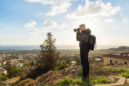 Travel, vacation, photographer and hitchhiker concept - traveler man photographed mountains and townの写真素材