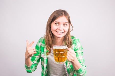 Cheerful young woman holding a beer mug full of beer and smiling on white backgroundの写真素材