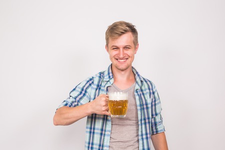 Cheerful young man holding a beer mug full of beer and smiling on white backgroundの写真素材