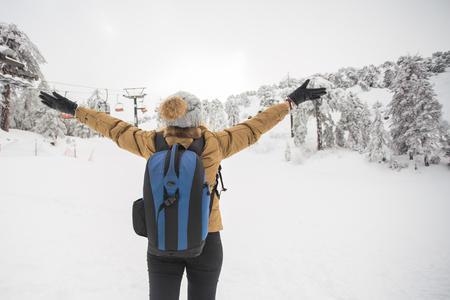 Happy girl standing back and hands up on winter nature background. Winter, vacation, weekend and freedom conceptの写真素材
