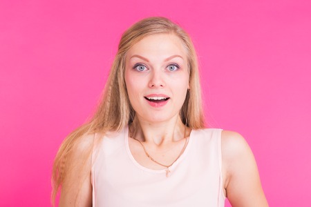 Surprised young woman over pink background. Looking at cameraの写真素材
