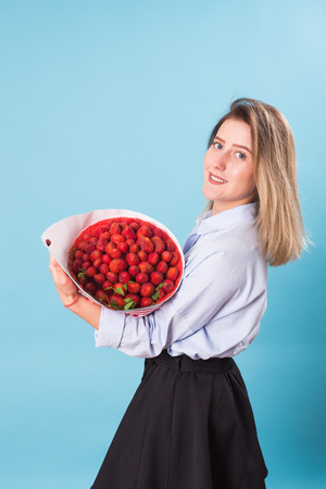 Young woman holding bouquet of strawberries on blue background.の写真素材