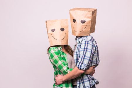 Love couple covering their faces with paper bag over white background.の写真素材