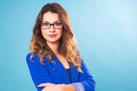Portrait of happy smiling young cheerful businesswoman in glasses over blue background. Caucasian brunette model in business concept studio shoot.の写真素材