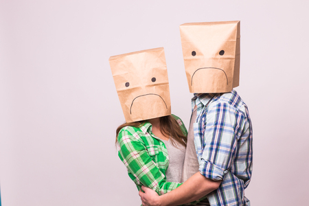 people, relationship difficulties, conflict and family concept - unhappy couple covering their sad faces with paper bag over white background.の写真素材