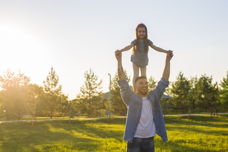Happy man holding his little daughter on neck in summer parkの写真素材
