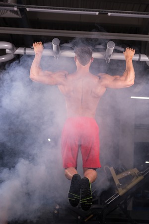 Athlete muscular fitness male model pulling up on horizontal bar in a gym.