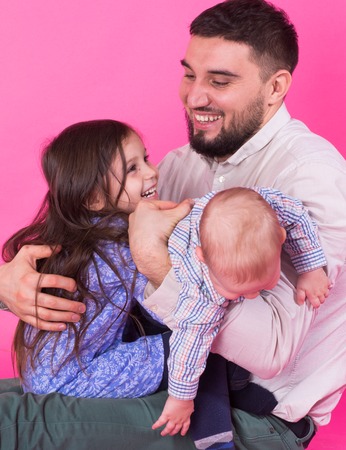 handsome father carrying his little daughter and baby son on pink backgroundの写真素材