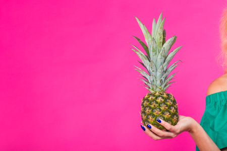 Closeup of womans hand holding pineapple over pink background with copyspace. Summer, diet and healthy lifestyle conceptの写真素材