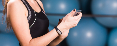 Close up of woman using cell phone and fitness tracker in gymの写真素材