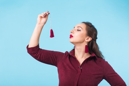 Young woman holding red earrings isolated on blue backgroundの写真素材