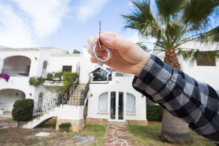 Holding house keys on house shaped keychain in front of a new home.の写真素材