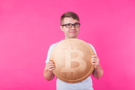 Portrait of smiling man with big bitcoin on pink backgroundの写真素材