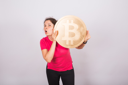 Funny young woman holding big bitcoin on white backgroundの写真素材