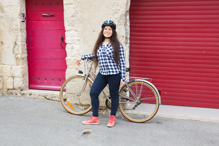 Young woman with bicycle looking camera on the background red doorsの写真素材