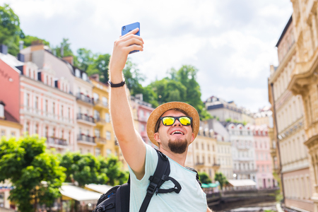 Handsome man taking selfie with mobile smart phone camera in european city. Vacation, travel and holiday concept.の写真素材