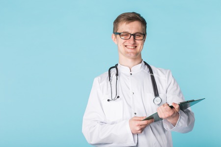 Portrait Of Male Doctor Writing On Clipboard Over a blue background with copy space