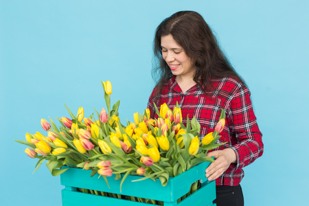 Young female florist with big box of yellow tulips over blue backgroundの写真素材