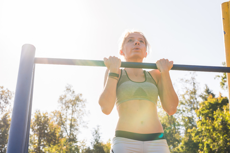 Young beautiful girl doing chin-ups on the outdoor sports groundの写真素材