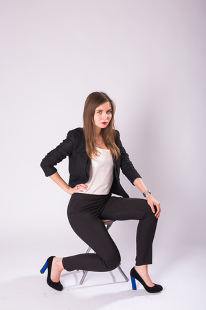 beautiful young business woman in black suit sits on a chair on white backgroundの写真素材