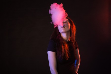 young woman smoking electronic cigarette on dark background