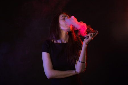 young woman smoking electronic cigarette on dark backgroundの写真素材