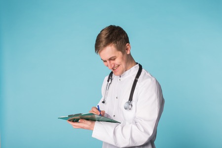 Portrait Of Male Doctor Writing On Clipboard Over a blue backgroundの写真素材