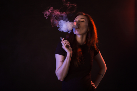 Portrait of asian woman smoking vape or e-cigarette in neon light at black background.の写真素材