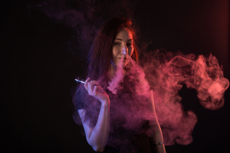 Portrait of asian woman smoking vape or e-cigarette in neon light at black background.の写真素材