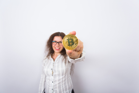 Cryptocurrency, virtual money and blockchain concept - Young funny woman holds a gold bitcoin in her hand.の写真素材